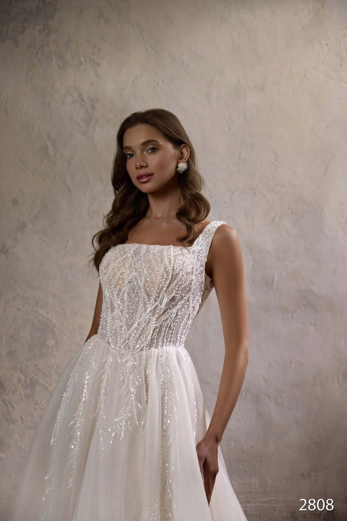 Aline wedding dress with basque waist and beaded bodice, featuring a built-in corset, model showcasing elegance.