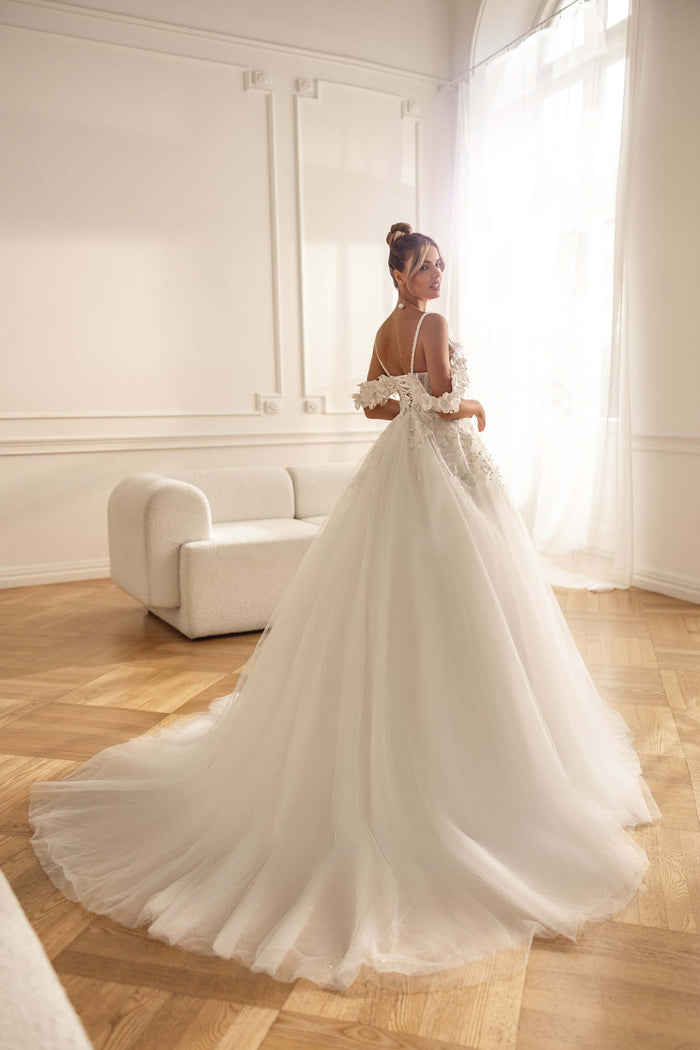Aline wedding dress with off shoulder straps and 3D lace, showcasing the back view and flowing train inside a bright room.