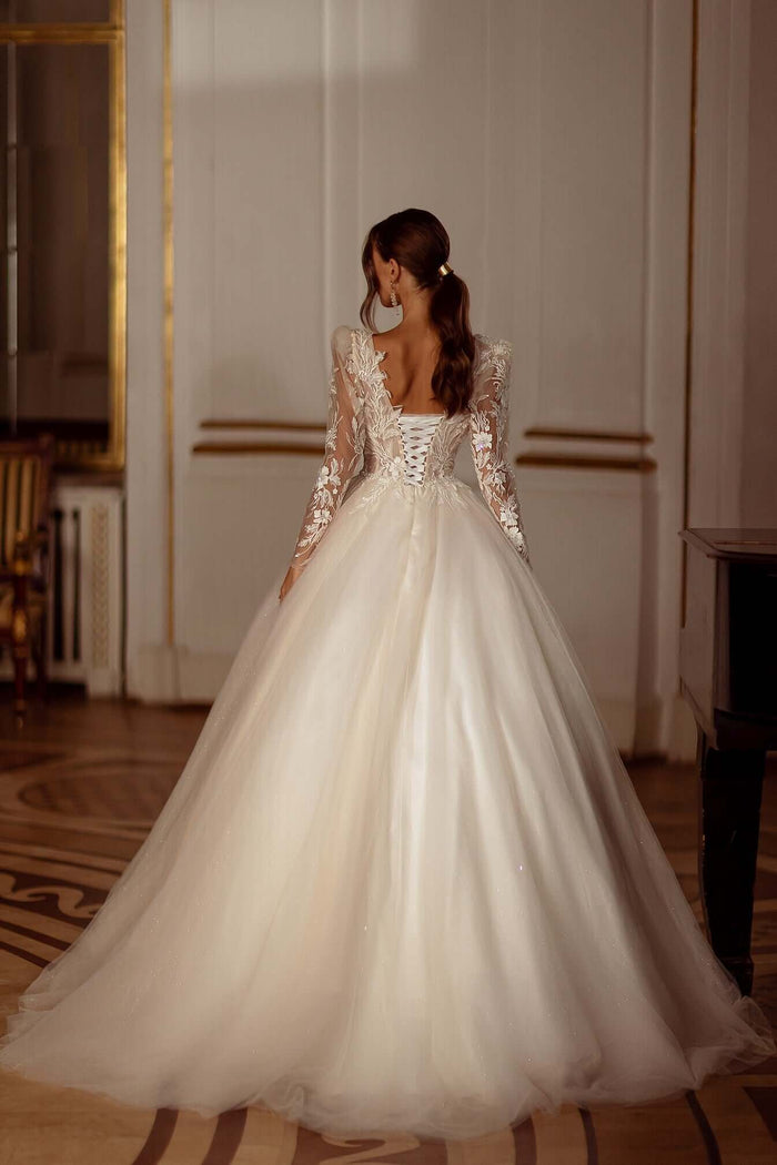 Aline wedding dress with fitted long sleeves and beaded lace, showcasing the back view and flowing skirt in elegant setting.