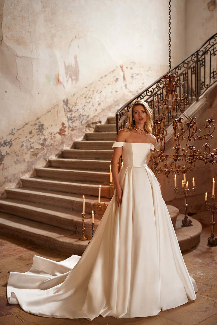 Margery - Simple Mikado Plain Satin Wedding Dress worn by model in elegant setting with stairs and candles.