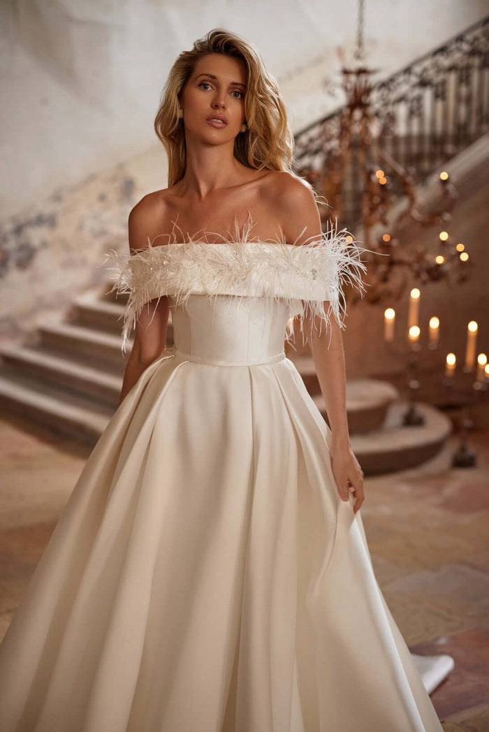 Model wearing Margery plain satin wedding dress with feathered off-shoulder detail on staircase.