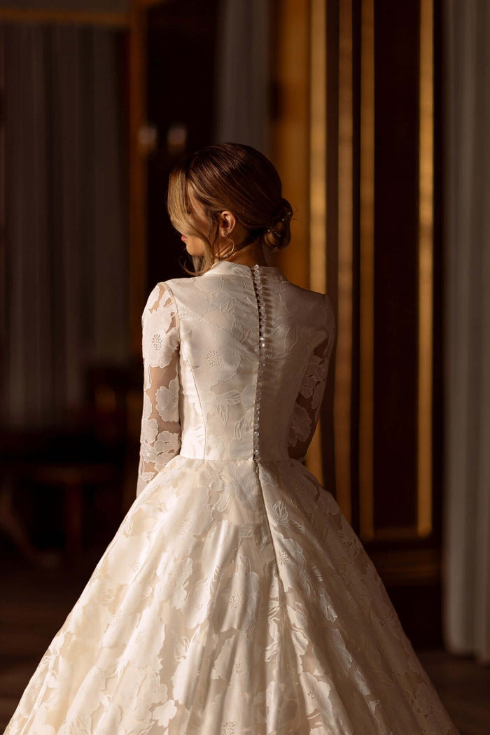 Back view of Raisa Aline Wedding Dress with long sleeves and floral lace fabric.