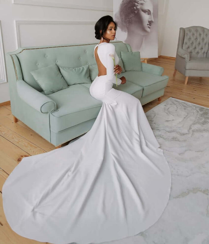 Stella - Crepe Fitted Wedding Dress - Size 6 displayed on a model sitting on a couch, showcasing the low back and cathedral train.