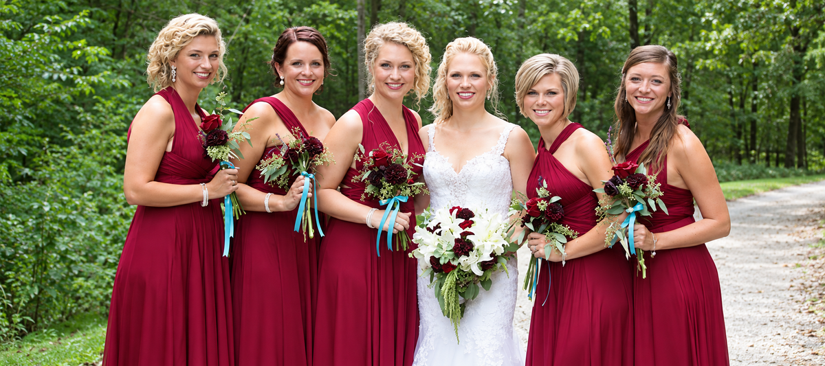 Bride with bridesmaids wearing burgundy infinity dresses outdoors
